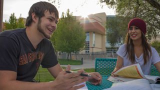 Image of two students sitting at a table outside talking.