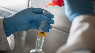 Image of chemistry experiment, adding a yellow liquid to a vial of clear liquid. 