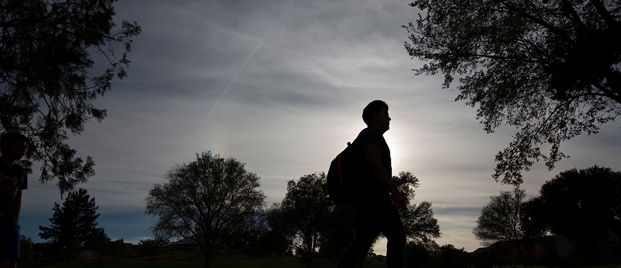 Image of silhouette of a student walking across campus.