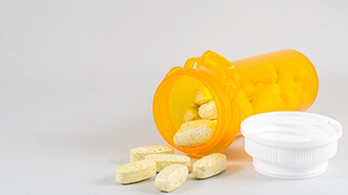 A bottle of prescription pill open and spilling onto a surface.