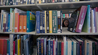 Image of two students through stacks of library books.