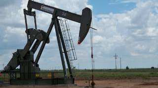 Image of oil pumpjack in the desert against a blue sky background.