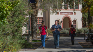 Image of two male students walking on the sidewalk. A tan adobe classroom building can be seen behind them. This is a link to the NMT Alternative Licensure Program