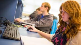 A red headed female student sits at a computer entering information.