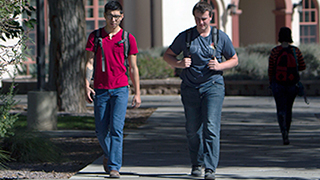 Two students are on campus talking and walking towards the camera.