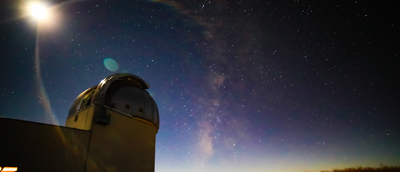 Image of the Magdalena Ridge Observatory telescope at sunset. The exterior view is from the ground looking towards the telescope, with stars in the background.