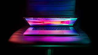 A laptop is partially opened on a chair in a dark room.
