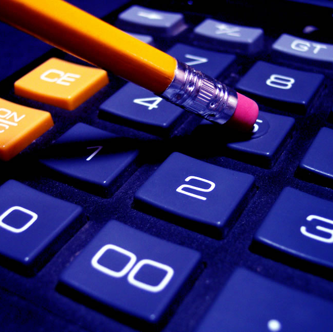 Close up image of a calculator and someone using the eraser end of a pencil to type numbers into the display.