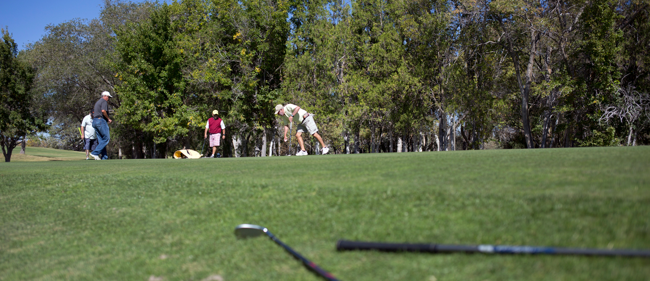 Image of four golfers in the distance, close up of golf clubs on the ground